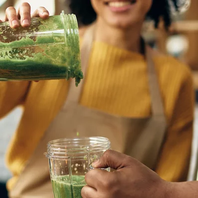 Gesunde Smoothies können helfen mit Vitaminen das Immunsystem zu stärken. Frau schüttet gesunden Smoothie in ein Glas in der Hand eines Mannes.