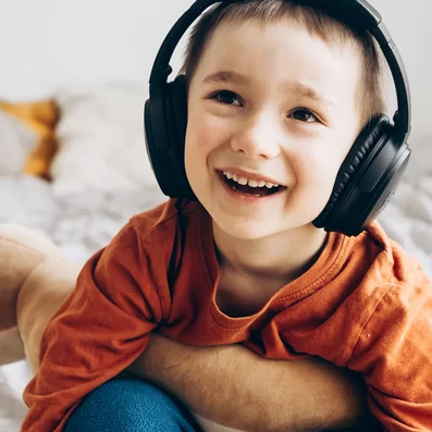 Wenn Kinder eine Erkältung haben, können Tipps gegen Langeweile, die Zeit angenehmer gestalten. Kind sitzt auf einem Bett und hat Kopfhörer auf.